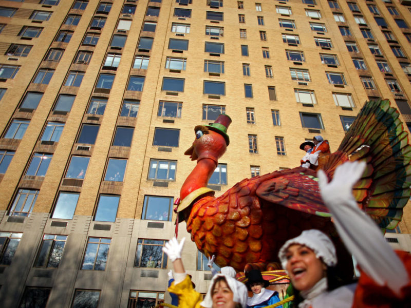 a giant inflatable turkey float in a parade with a large apartment building in the background