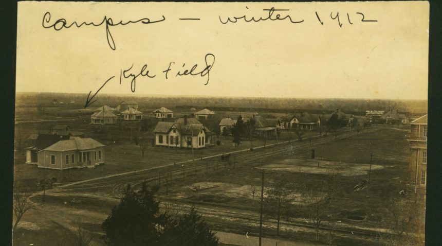 an old photograph showing a cluster of small houses and an athletic field in the back ground. handwriting at the top reads 