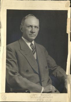 a black and white portrait of a older man in glasses and a grey suit. writing in pencil along the border says "E.J. Kyle, District Director, January 1934"