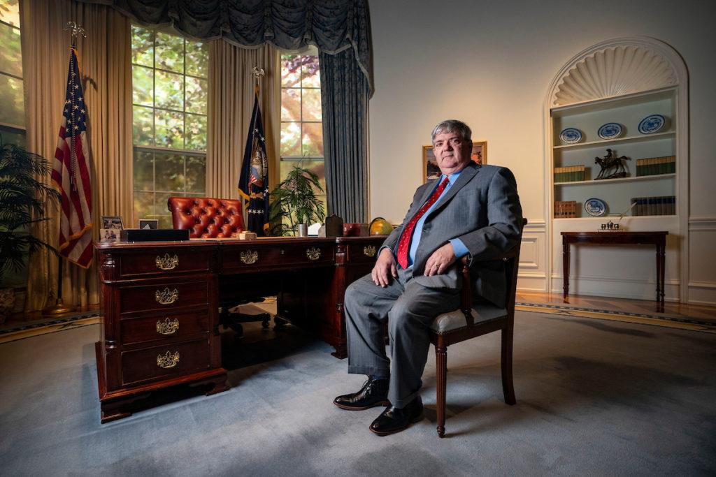 Warren Finch seated in a chair in an exhibit replicating the Oval Office in the White House