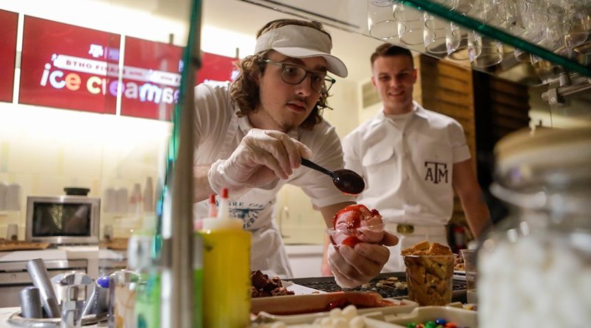 A Yell Leader looks on as an employee spoons strawberry syrup and other toppings onto a sundae