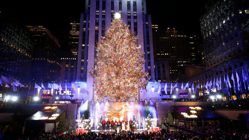 Photo taken at the 2022 Rockefeller Center Christmas Tree lighting, with performers on a stage below the tree
