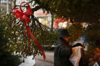 A bunch of mistletoe tied with red ribbon hangs in a stall at a christmas market, with shoppers in the background