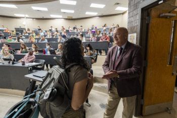 Jeffrey Savell stands at the front of a teaching theater filled with students speaking to a young woman wearing a backpack