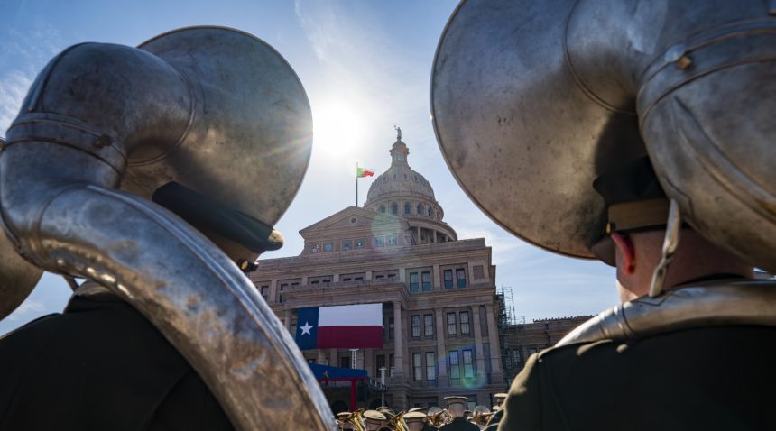 a photo from behind two sousaphone players with the state capitol building framed between their instruments