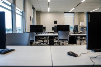 a photo of a computer lab, showing rows of desks with computer monitors and mice. west campus can be seen outside a couple of windows on the left side of the frame