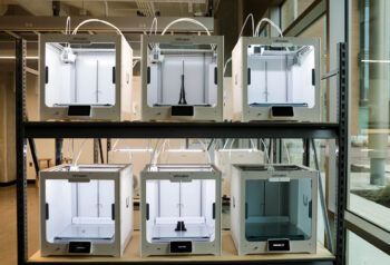 a photo of a shelf full of 3D printers, some of which have black printed objects inside of them