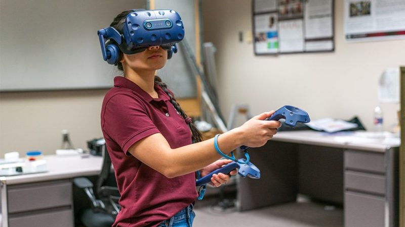 a photo of a woman in a maroon polo using a virtual reality headset and controllers