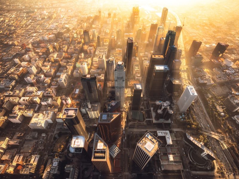 Downtown Los Angeles during a hazy sunset from a helicopter. The light rays shine gold from in between the building of DTLA.