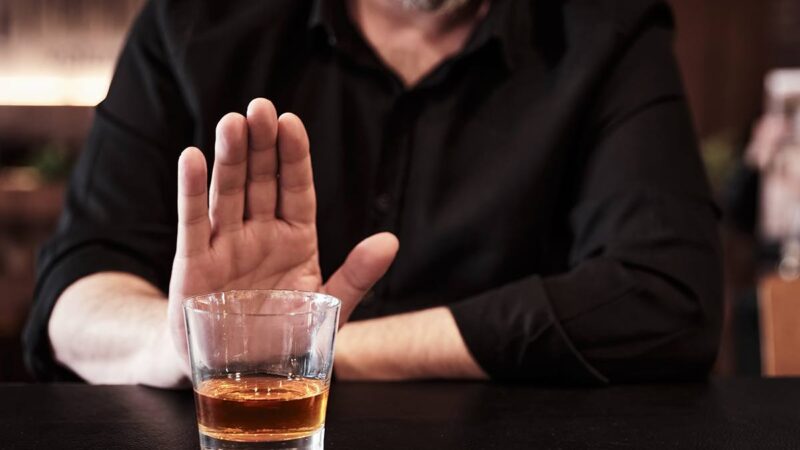 A man holding his hand up in front of a glass of alcohol
