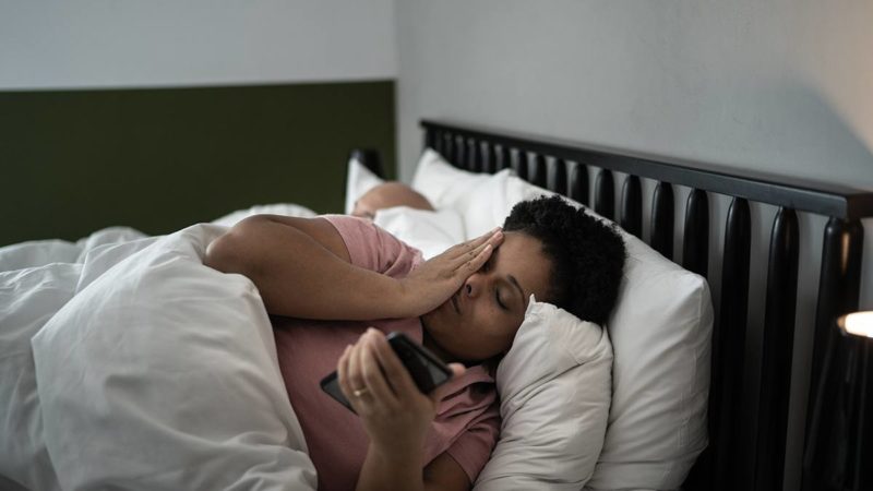 a woman lies awake at night while her husband sleeps beside her