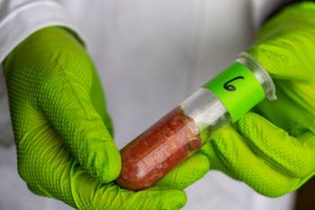 Close-up shot of someone wearing bright green gloves holding a vial containing raw meat