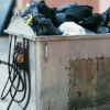 a photo illustration of a gas pump connecting a car to a dumpster full of garbage