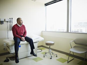 Mature male patient sitting on exam table looking out window in clinic room
