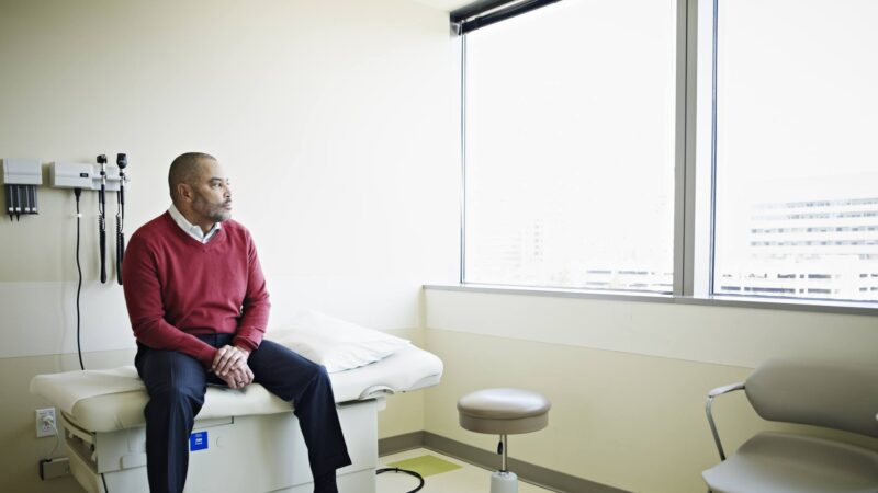 Mature male patient sitting on exam table looking out window in clinic room