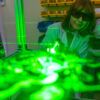 A green laser illuminates aerosolized particles with Dr. Maria King watching in the background