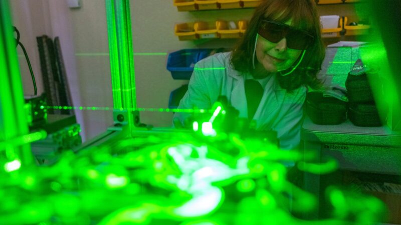 A green laser illuminates aerosolized particles with Dr. Maria King watching in the background