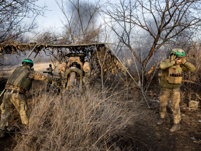 a photo of two people in military uniforms firing a large howitzer gun from a camouflaged position in the Ukrainian countryside