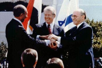 Jimmy Carter stands in between two men in a triple-handshake on the White House lawn