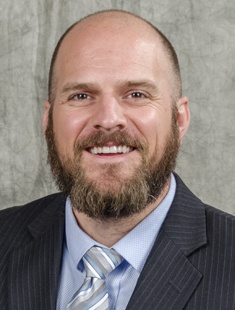 a headshot of a bearded man in a suit