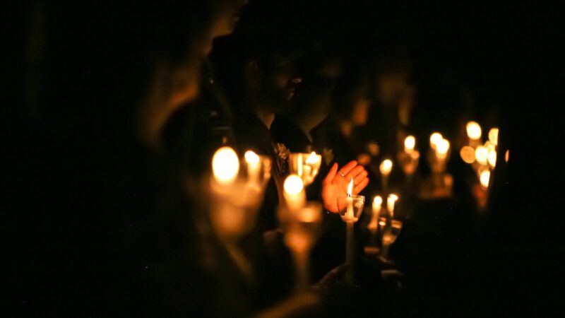 People in a darkened room hold candles that illuminate their faces