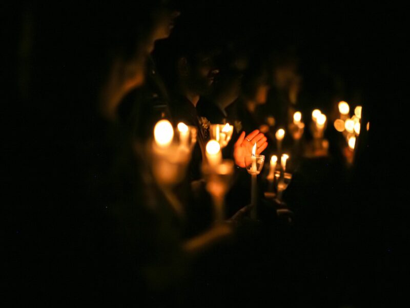 People in a darkened room hold candles that illuminate their faces