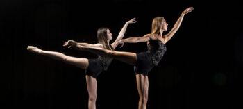 Two dancers posed in arabesque against a black background