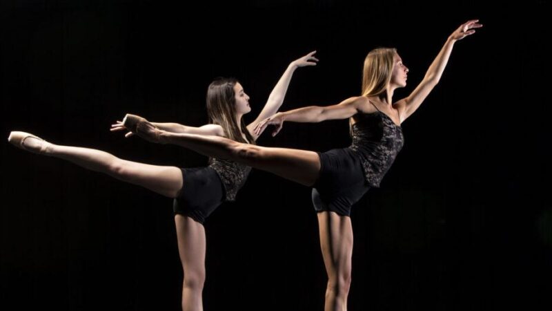Two dancers posed in arabesque against a black background