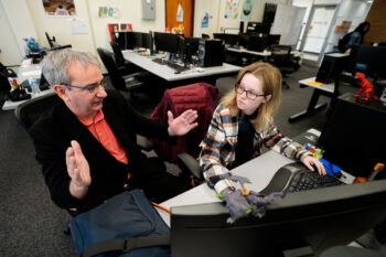 a photo of a professor sitting next to a college student at a computer