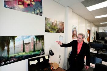 a photo of a professor pointing to various art prints on the wall, each showing a different colorful setting