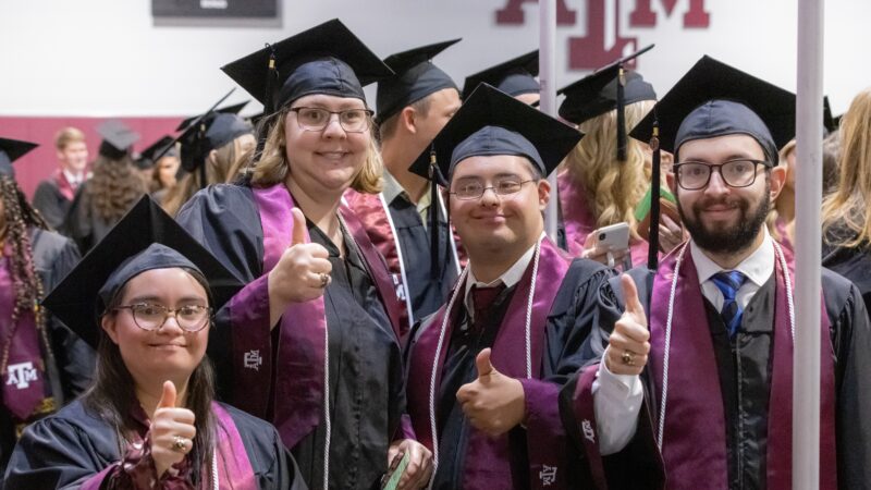 a photo of four people in graduation caps and gowns giving a thumbs up