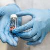 Close-up photo of two gloved hands holding a small vial of medication