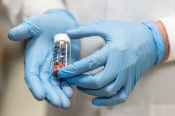 Close-up photo of two gloved hands holding a small vial of medication