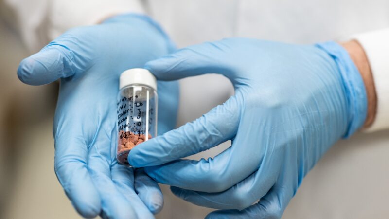 Close-up photo of two gloved hands holding a small vial of medication