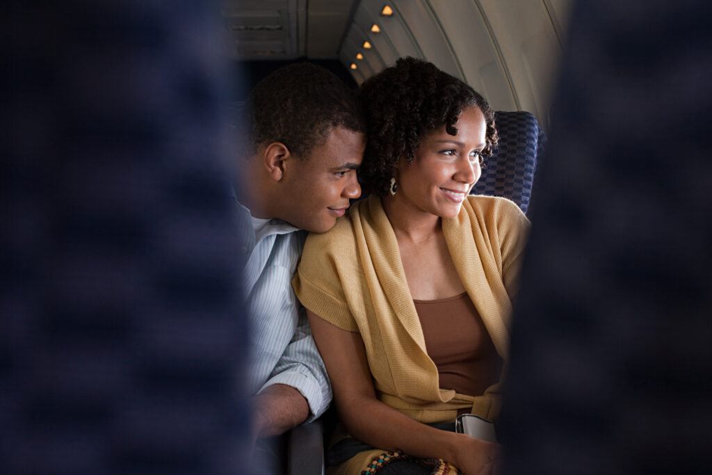 A couple seated next to each other on an an airplane look out the window