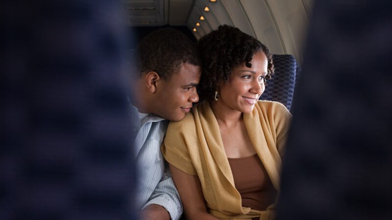 A couple seated next to each other on an an airplane look out the window