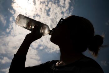 a photo of a young woman in silhouette, sipping from a clear plastic water bottle