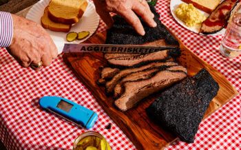 cutting a brisket with a knife that says Aggie Brisketeers