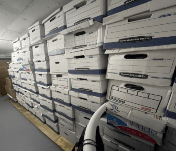 Dozens of boxes stacked up to the ceiling against a wall in a storage room