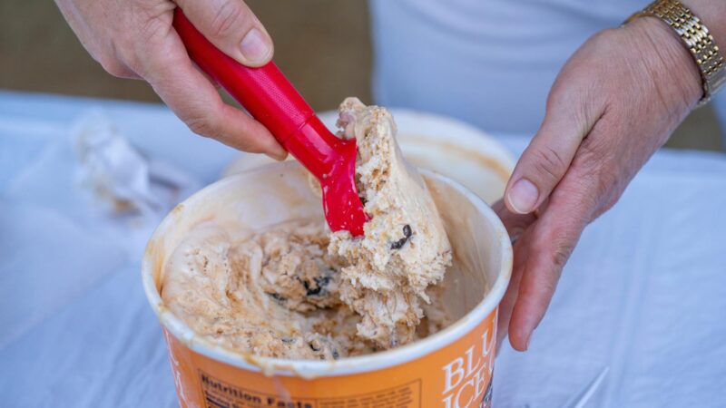 A person scoops ice cream from a half-gallon container.
