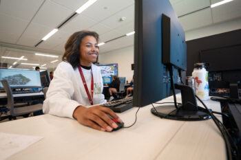 a photo of a young woman using a computer in a computer lab while smiling