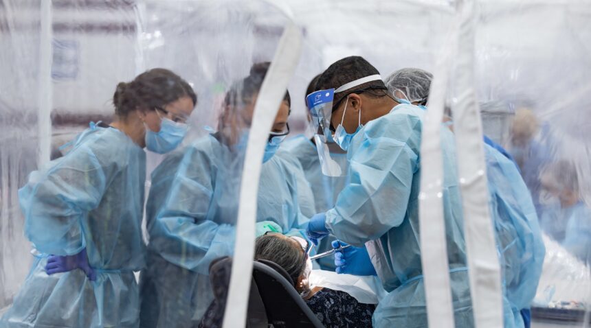 a group of several people in scrubs tending to a dental patient in a plastic tent