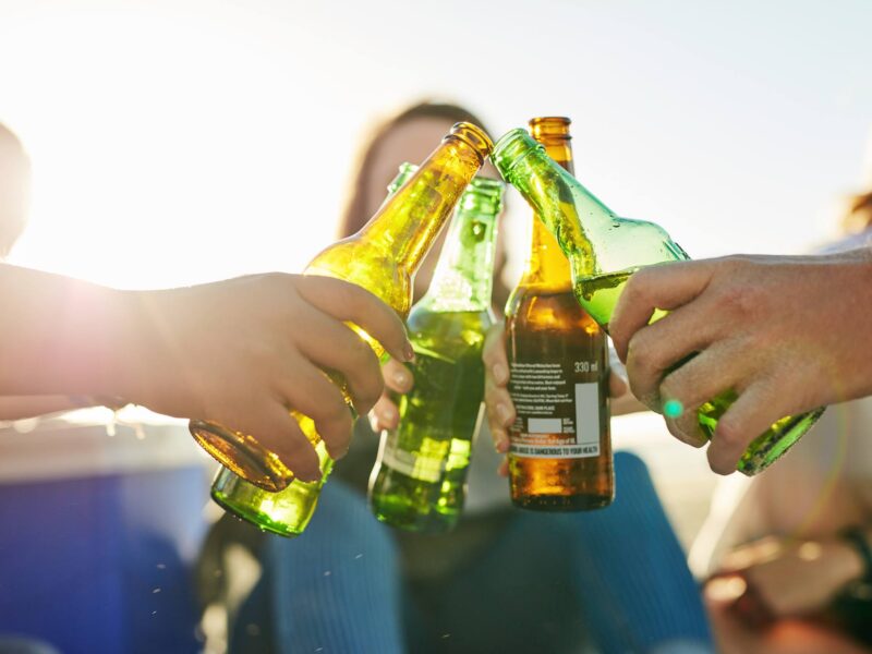 Shot of young people spending a summer’s day outdoors, clinking bottles of beer together