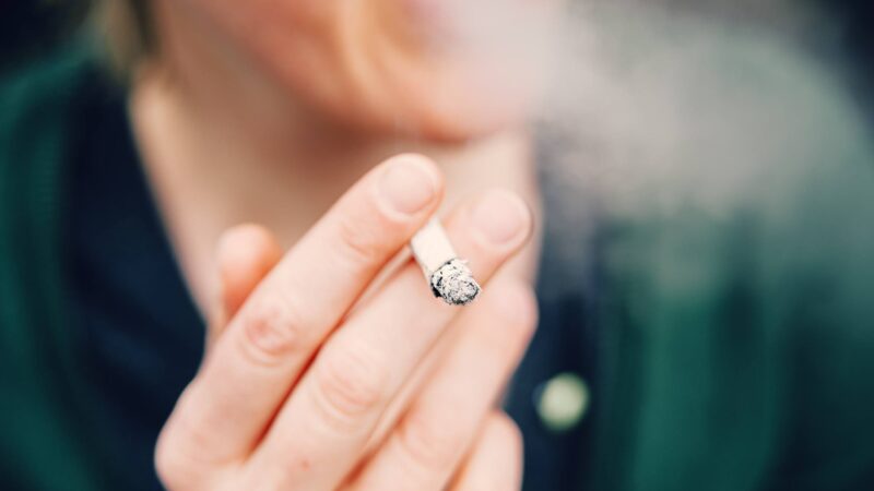 Unrecognizable woman wrapped in cigarette smoke holding a lit cigarette in her hand