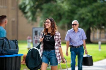 a student and family member bringing luggage on to campus