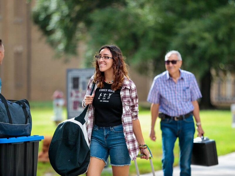 a student and family member bringing luggage on to campus