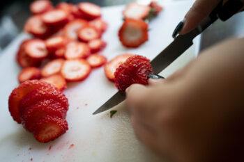 Close up of someone cutting slices of strawberry on a cutting board