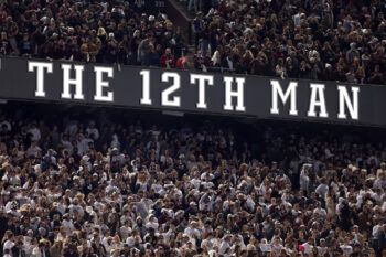a photo of fans packing Kyle Field for a football game with lettering reading "THE 12TH MAN" dividing two decks of seating