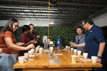 Eric Brenner stands around a table giving a coffee demonstration to center visitors