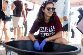 a photo of a young woman in sunglasses crouching next to a bucket and smiling
